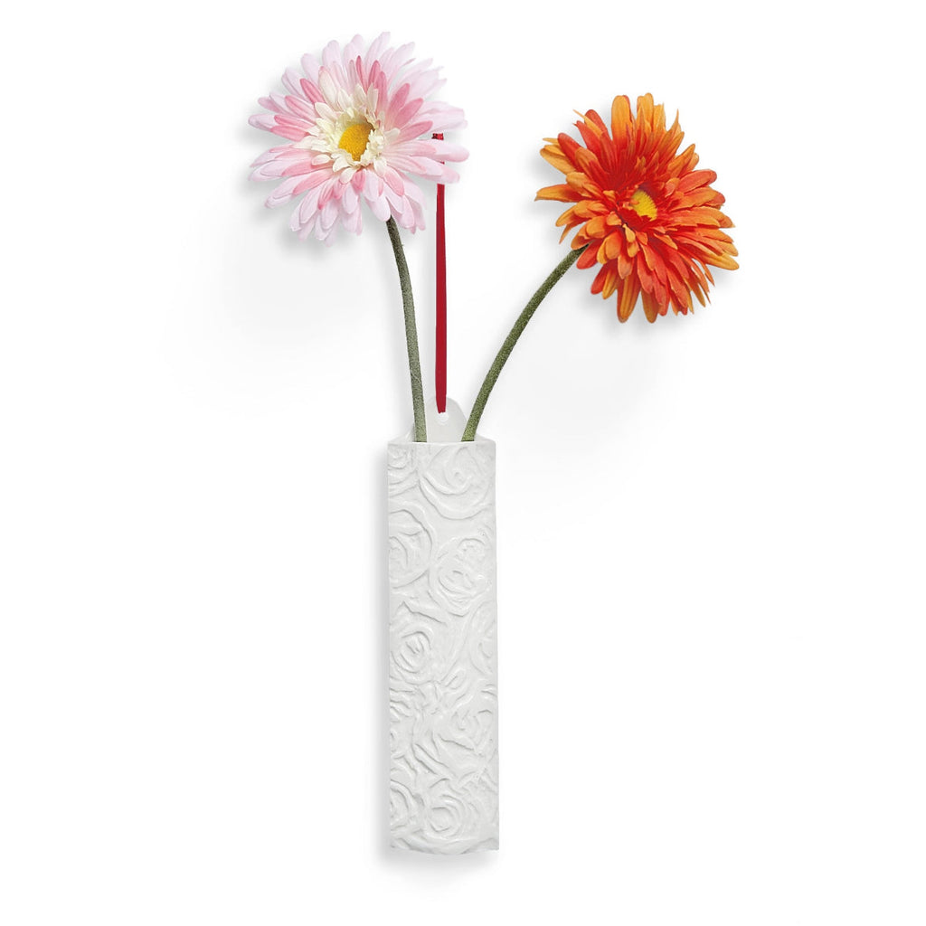 White hanging wall vase with embossed pattern holding pink and orange daisy flowers