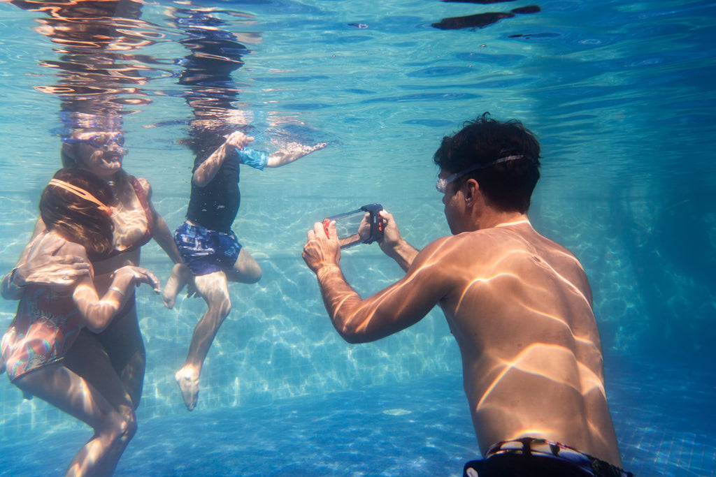 Waterproof phone case held underwater with clear front window and orange button controls.
