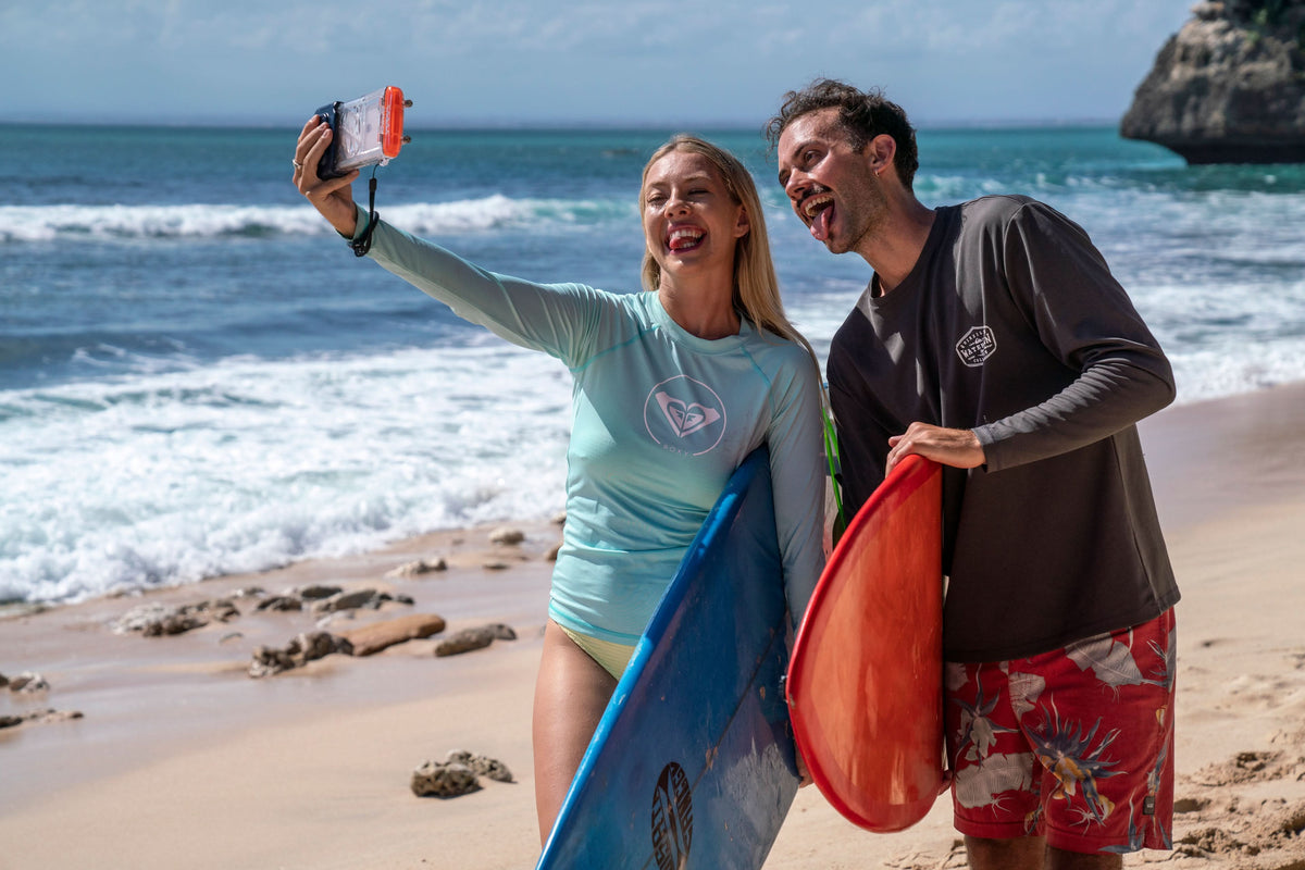 Waterproof phone case with clear front and orange trim, carried near the ocean.