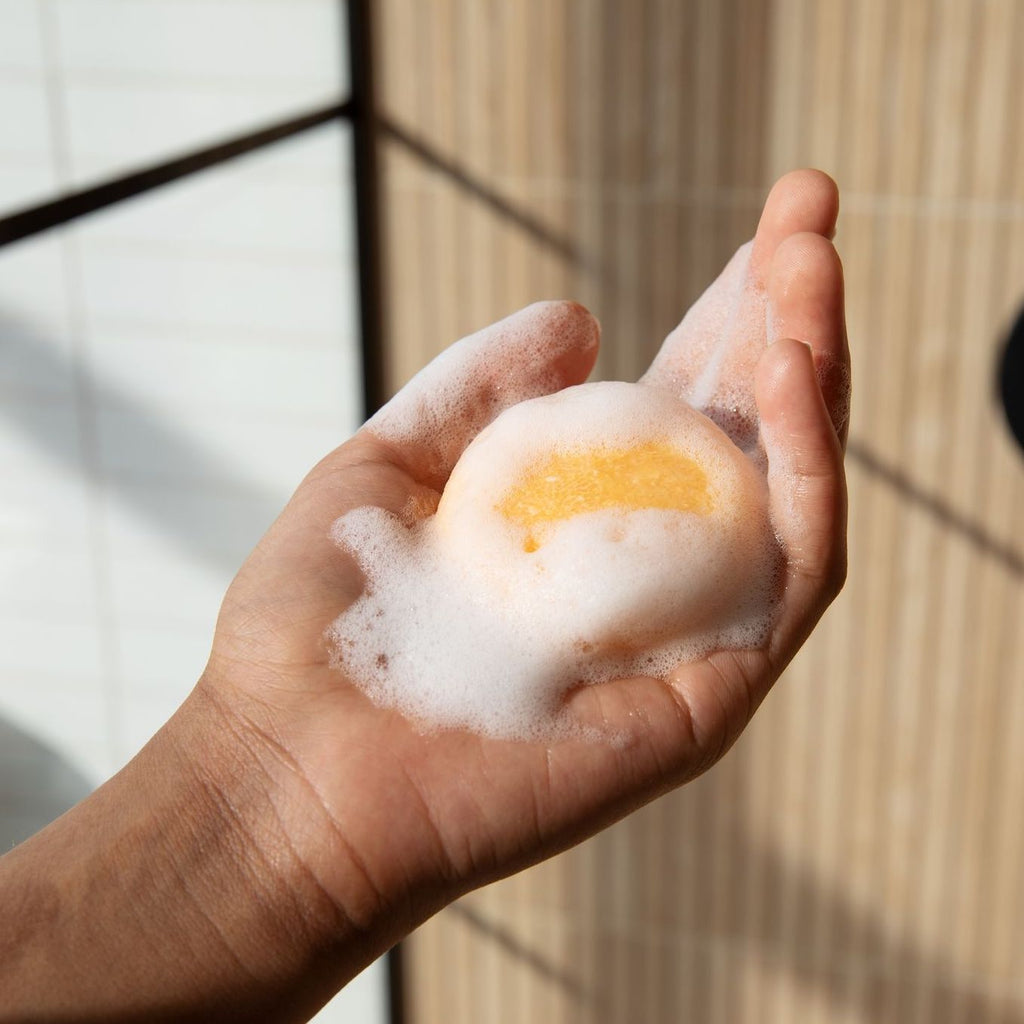 Hand holding peach moisturizing shampoo bar covered with white lather