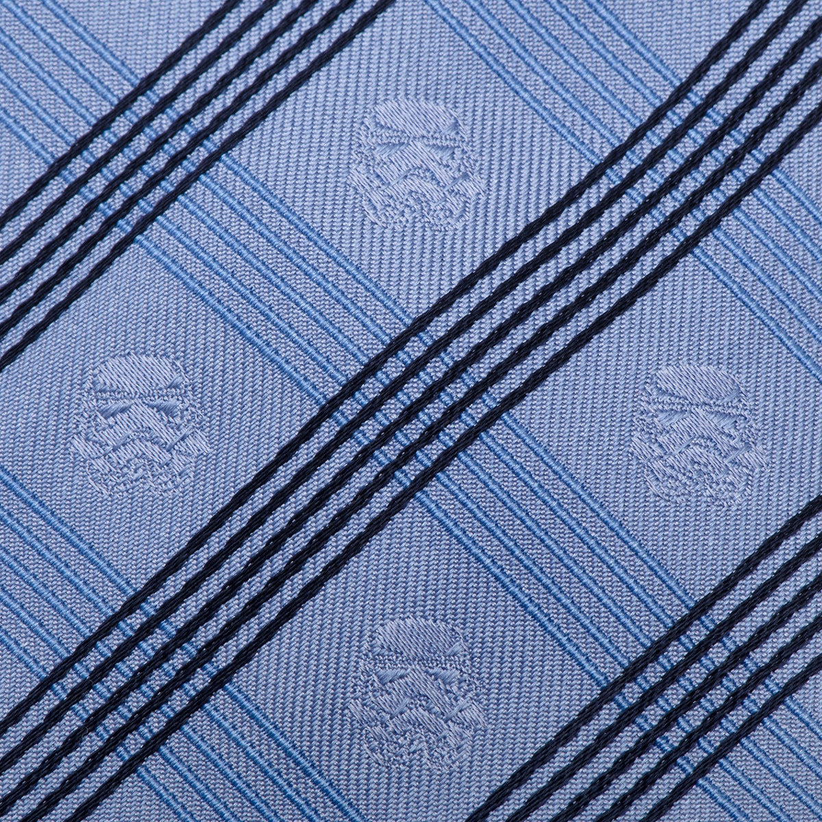 Close-up of light blue plaid necktie fabric with diagonal dark stripes and emblems