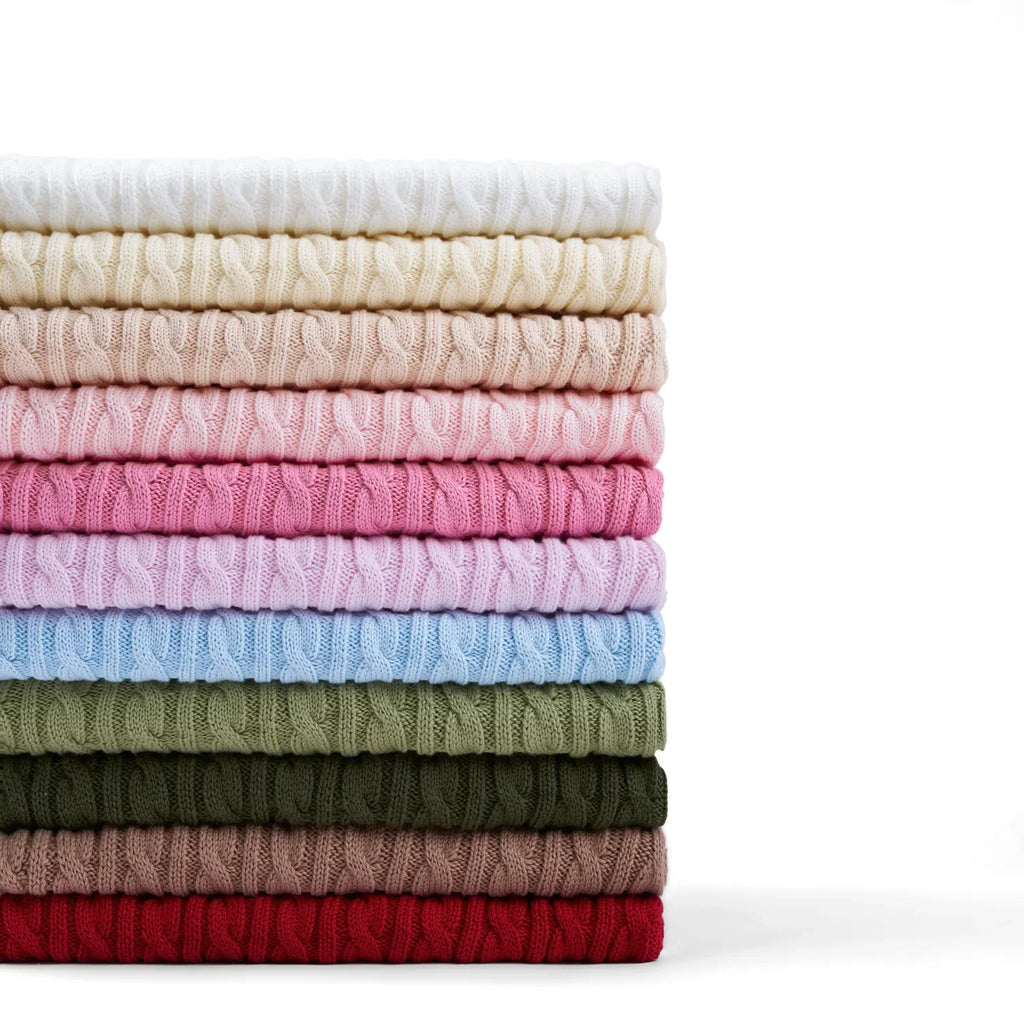 Stack of folded baby cable-knit sweaters in pink, blue, white, green, and red