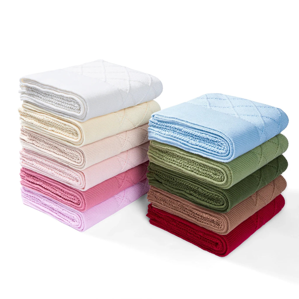 Stack of knit baby blankets in multiple colors with diamond-stitch pattern