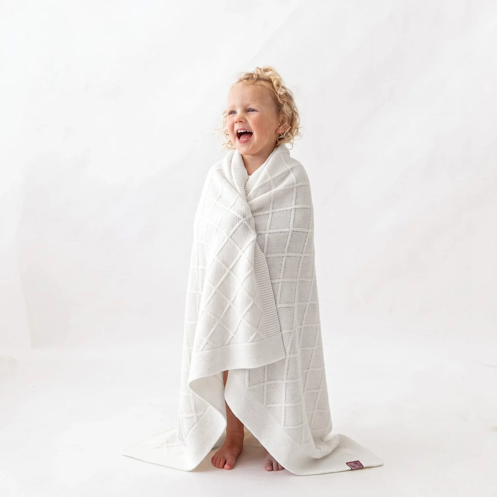 White diamond-stitch knit baby blanket draped around a baby for cuddling
