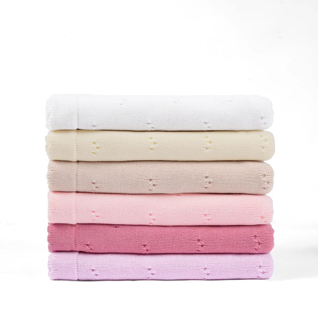 Stack of pointelle knit baby blankets in white, cream, tan, blush, and pink shades