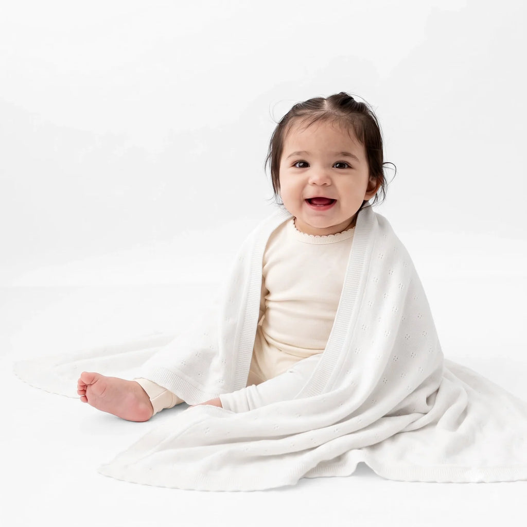Pointelle baby knit blanket in white, draped over a toddler for wrapping or swaddling.