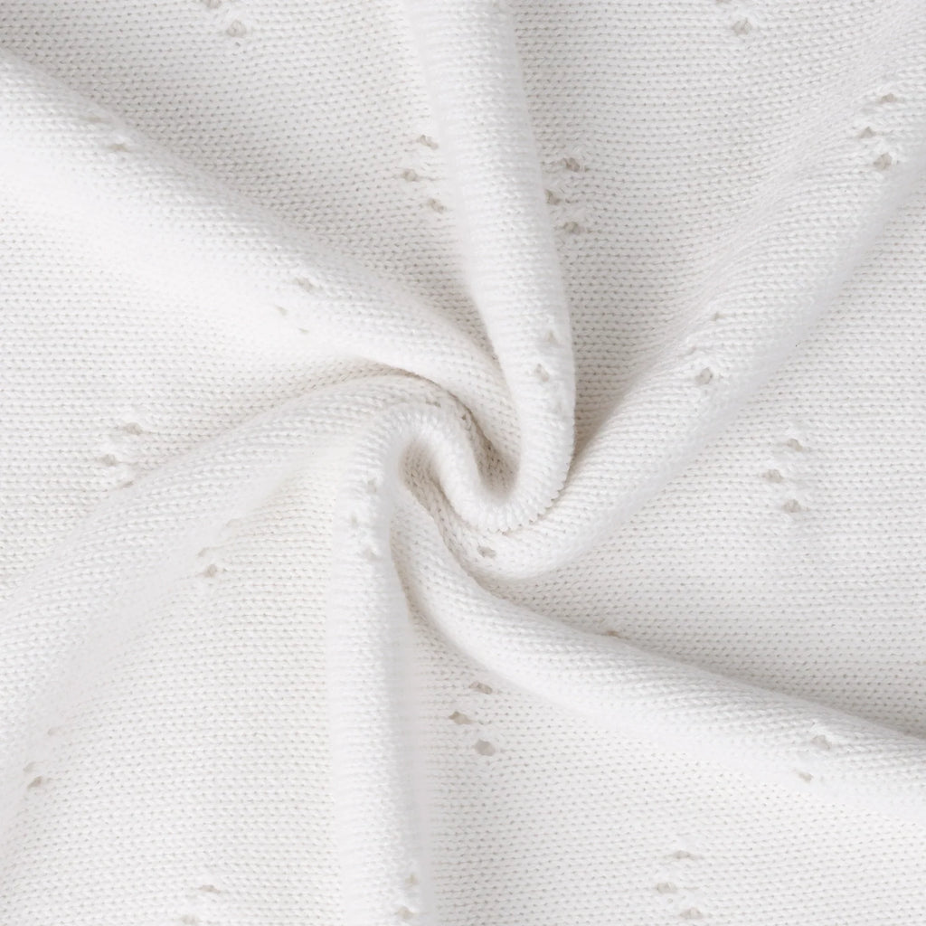 Pointelle baby knit blanket close-up with white textured eyelet dots and soft draped folds.