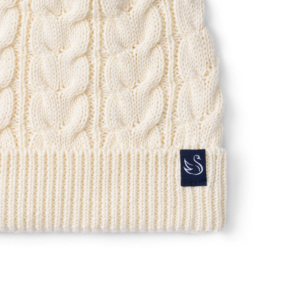 Cream cable-knit beanie with ribbed cuff and navy logo patch near hem