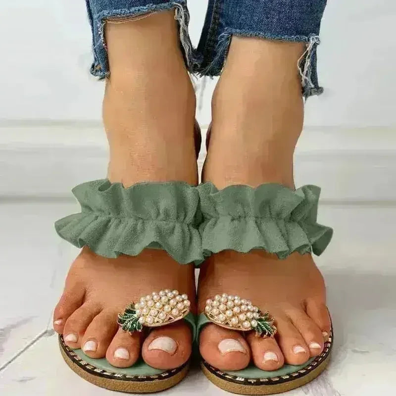 Green flat toe sandals with pearl pineapple ornaments and ruffled strap on feet