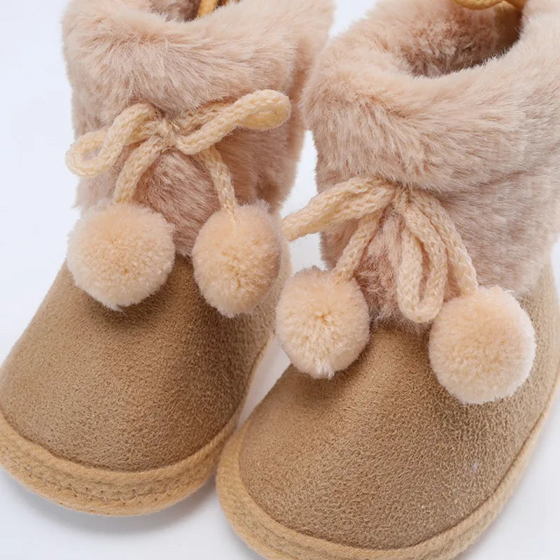 Baby booties with fuzzy lining, bow laces, and pompom charms; tan close-up