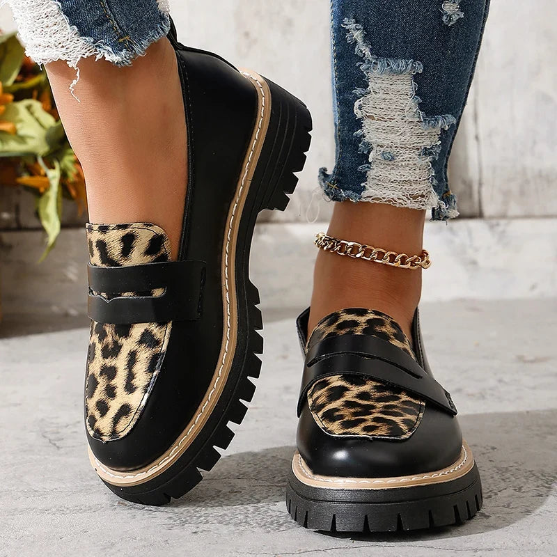 Two black platform loafers with leopard print panels and thick lug soles.