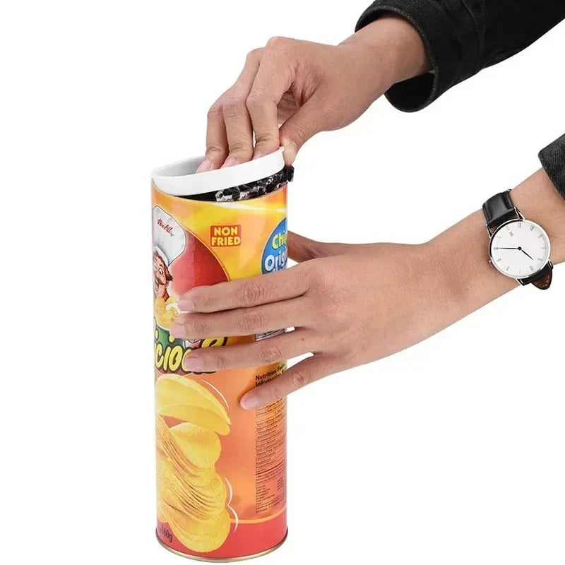 Chip can with white rim and coiled snake spring toy being inserted by hands.