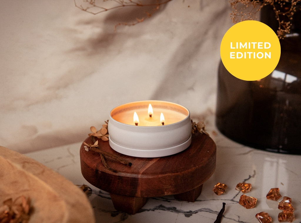 Lit three-wick candle in a white jar on a round wooden base
