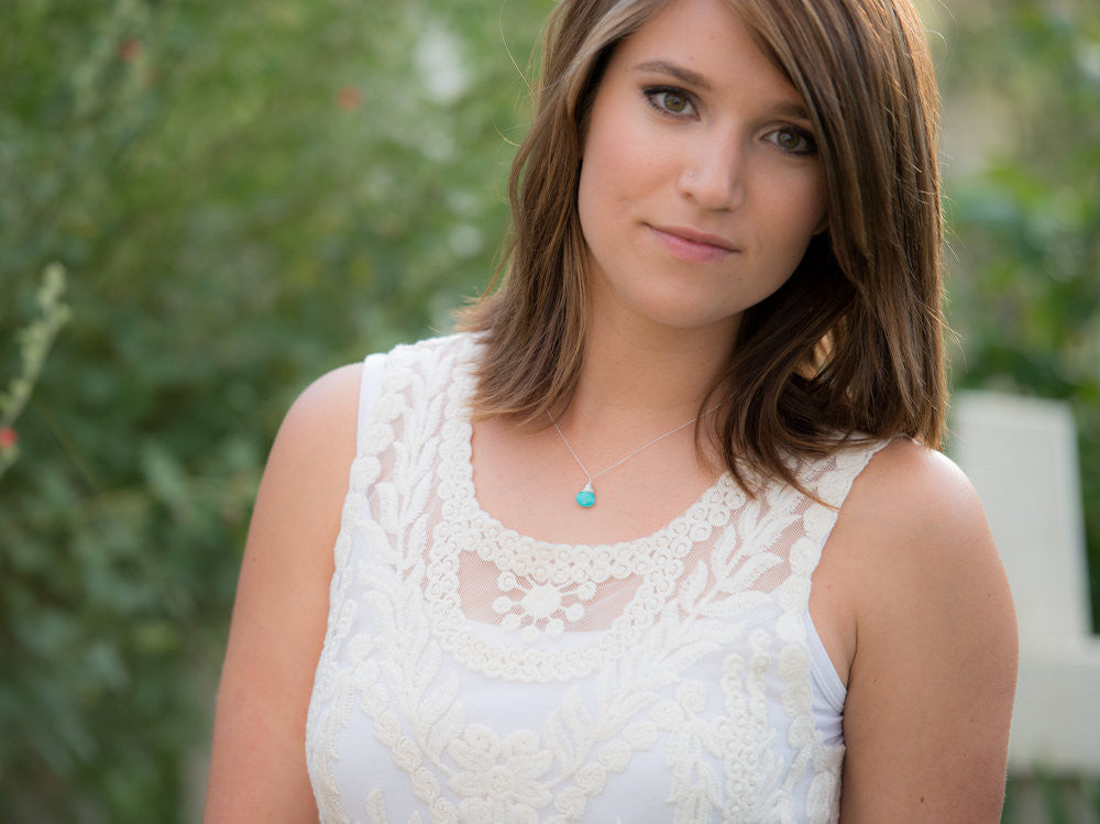 Turquoise solitaire pendant necklace worn on a woman with a white lace top