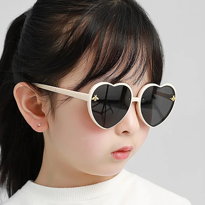 Heart-shaped kids sunglasses on a child with white frames and dark tint lenses