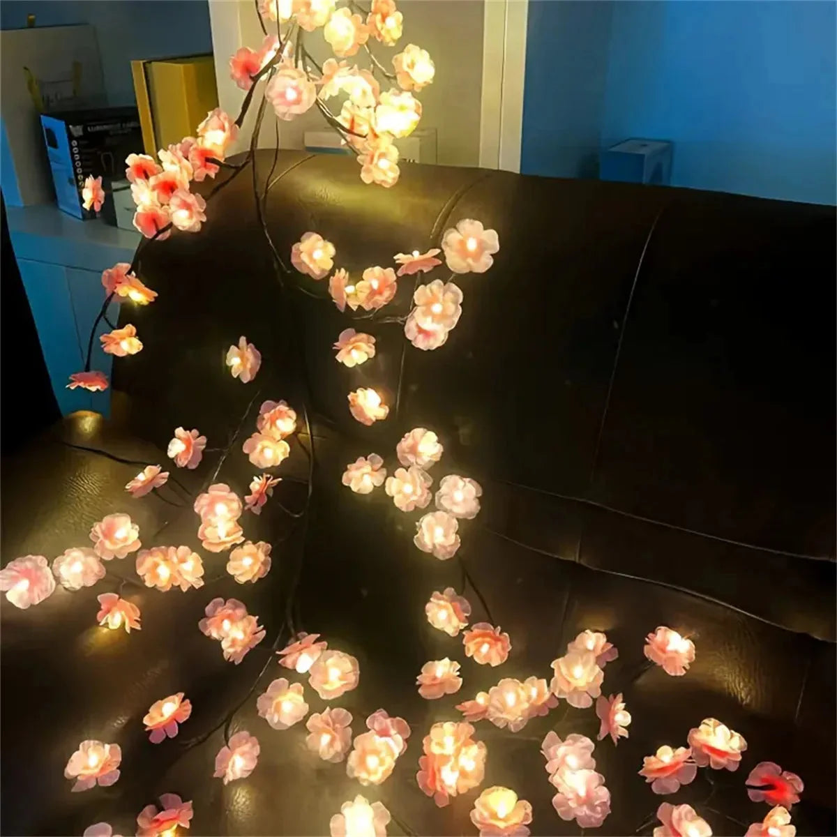 Cherry blossom branch LED lights draped across sofa back, warm white bulbs