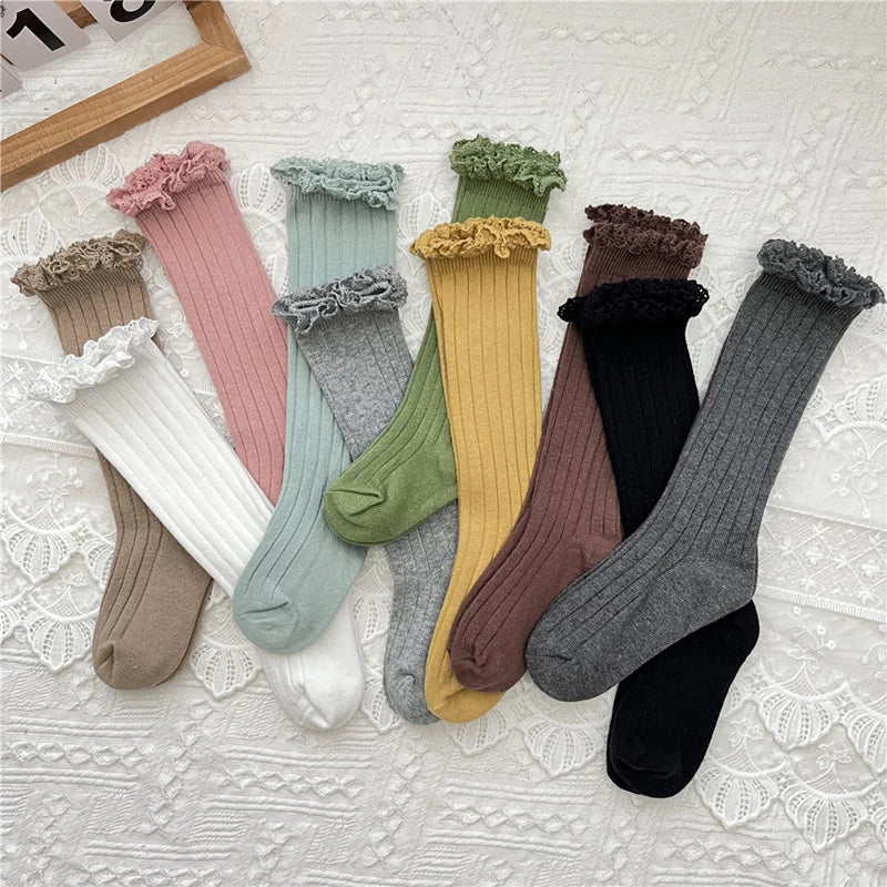 Assorted knee-high lace cuff socks with ruffles, mixed colors laid on fabric