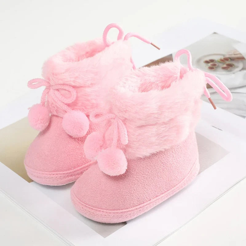 Baby winter booties with plush lining, bow ties, pompom trim, and soft sole; pink