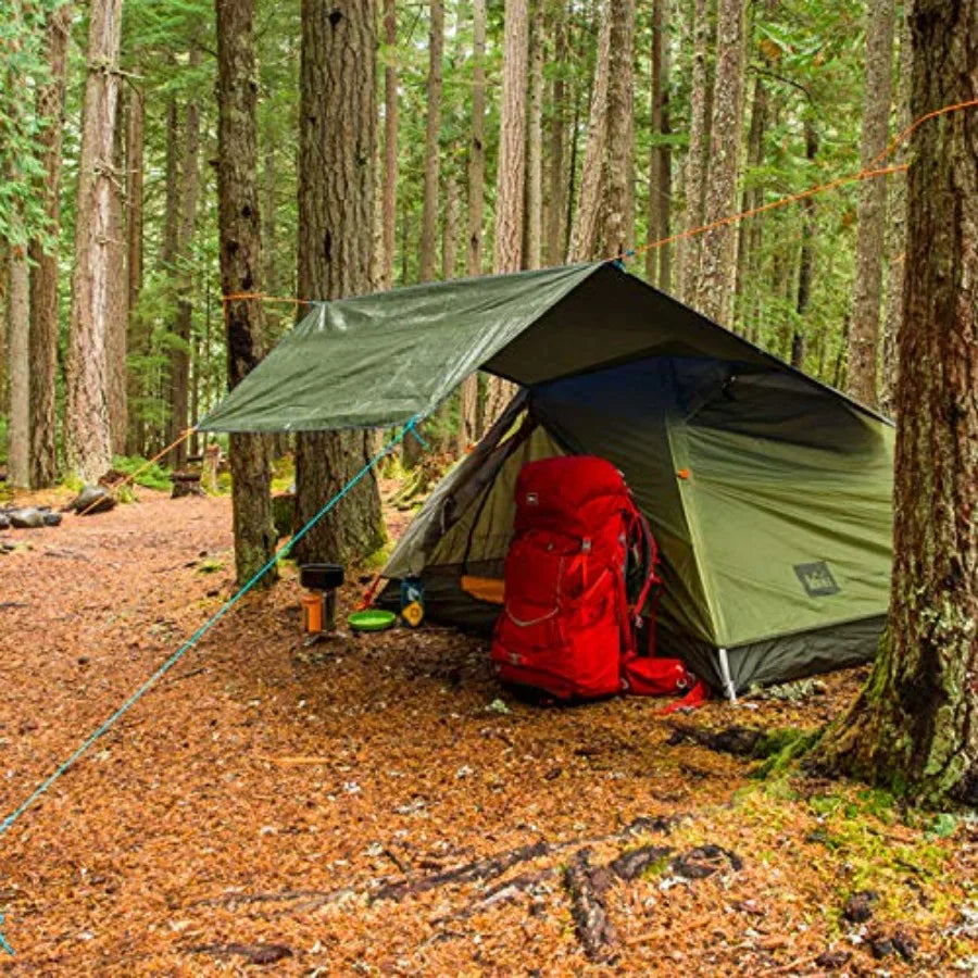 Green tarpaulin cover used as shelter over a camping tent in the woods