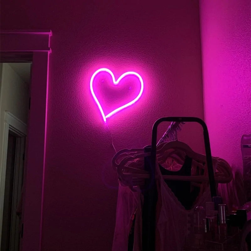 Pink glowing heart neon wall sign on a wall above a cabinet and decor