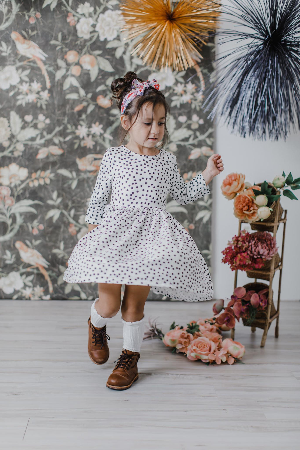 Girl wearing a white polka-dot twirl dress with 3/4 sleeves and bow headband