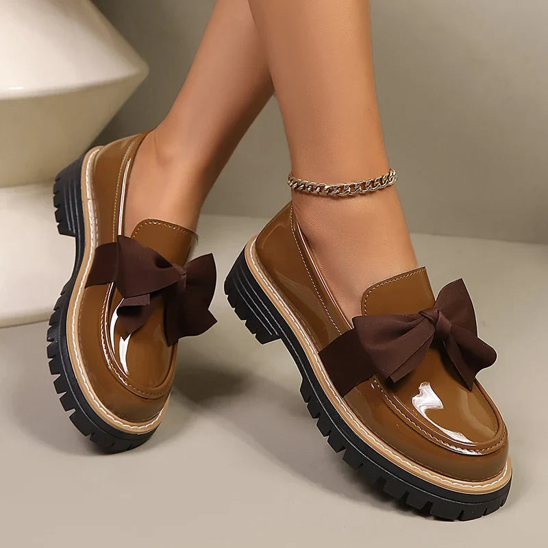 Brown slip-on loafers with dark bow detail; thick platform sole with contrast stitching.