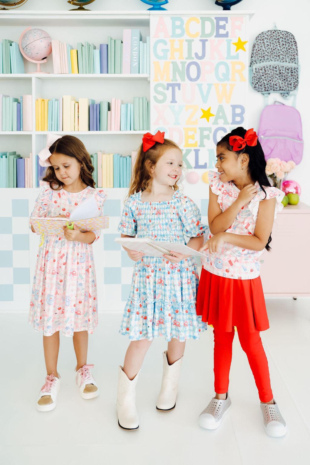 Group wearing printed ruffle twirl dresses with 3/4 sleeves and colorful bow motifs