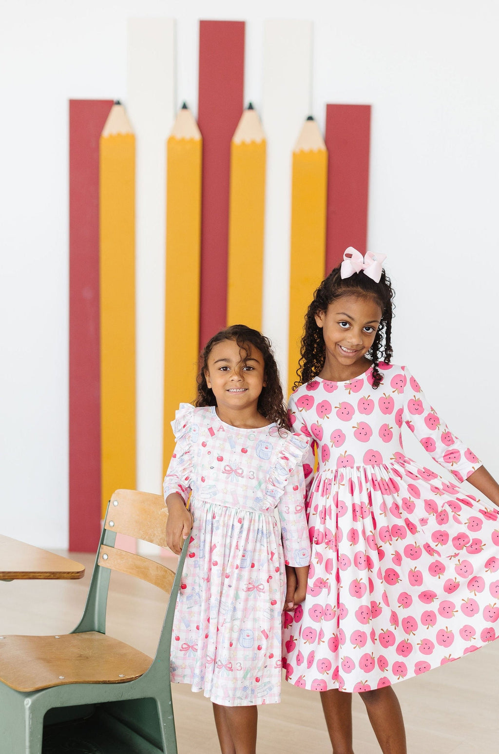 Two kids wearing printed 3/4 sleeve ruffle twirl dresses, one white and one pink