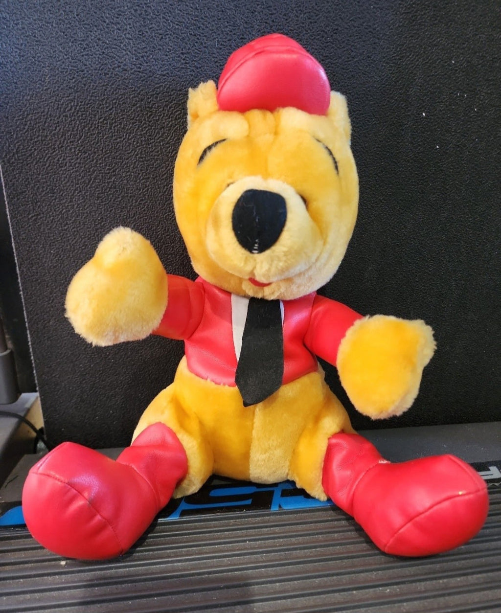 Plush Winnie-the-Pooh bear in red racing outfit, seated with black tie