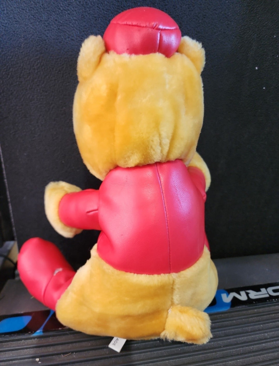 Plush Winnie-the-Pooh bear rear view in red racing outfit with padded helmet