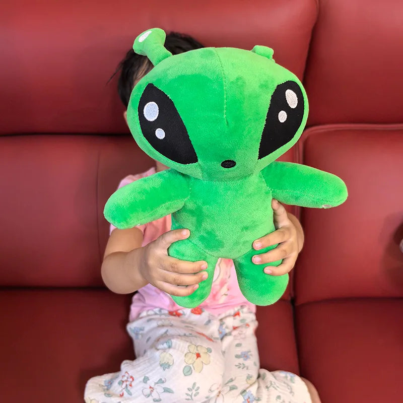 Green alien plush toy held in front of chest, round head with horn tentacles