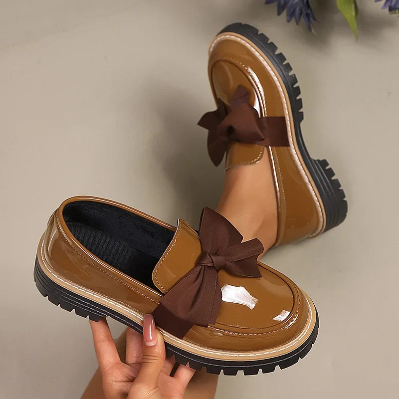 Brown patent loafer with dark bow and platform lug sole; open top shows dark lining.