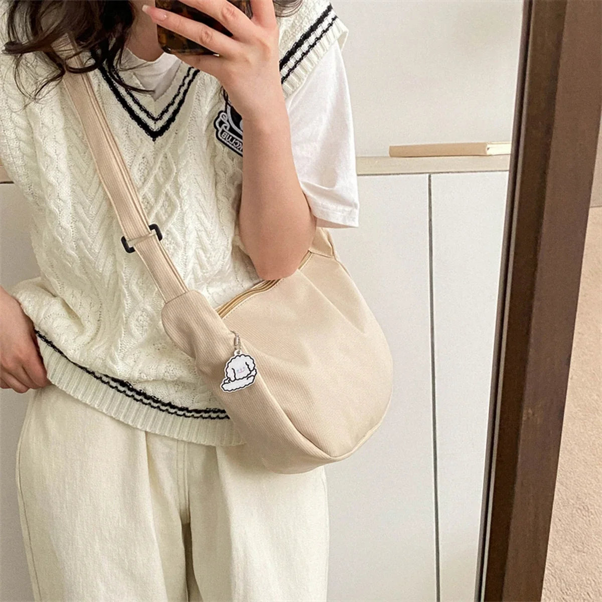 White crossbody bag worn with puppy pendant and adjustable shoulder strap, zip-top