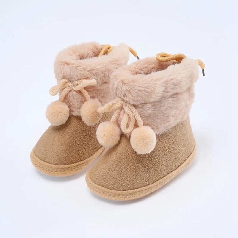 Baby tan booties with fuzzy lining, bow laces, and pompom trim; soft sole