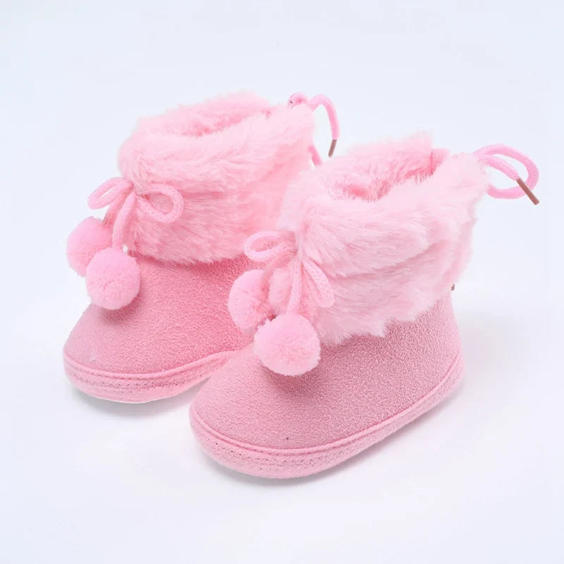 Baby pink winter booties with plush lining, lace bow ties, and pompom accents