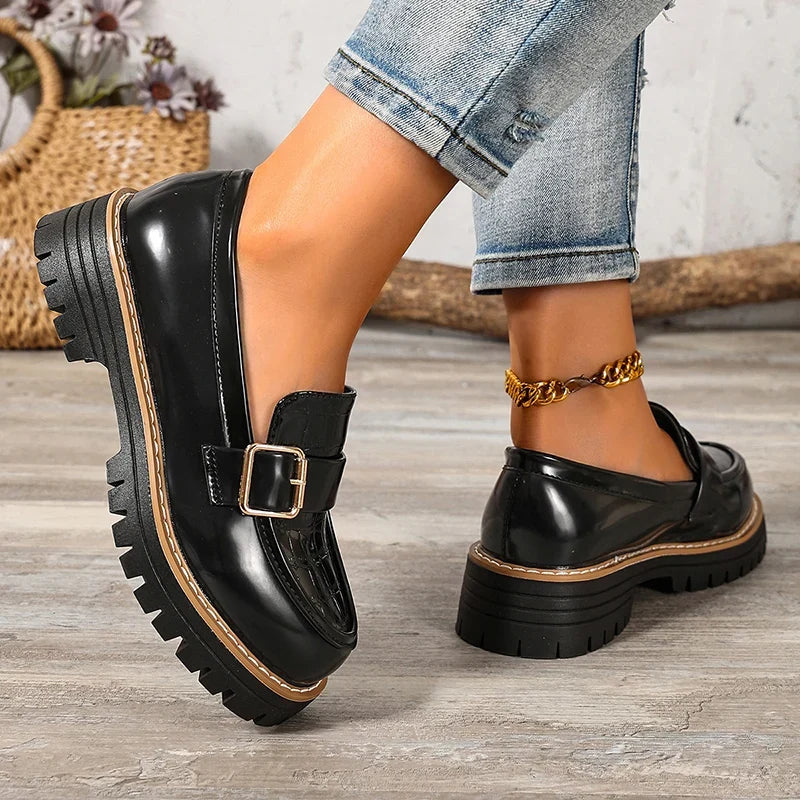 Black patent leather platform loafers with buckle strap and thick lug sole, angled view