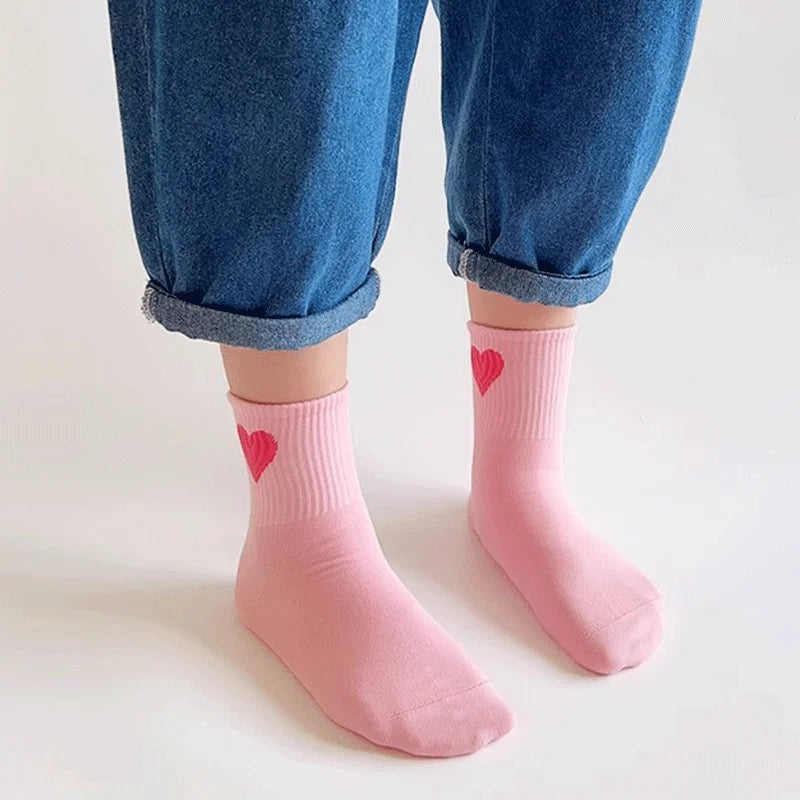 Girls pink mid-calf socks with red heart pattern, worn with blue denim pants