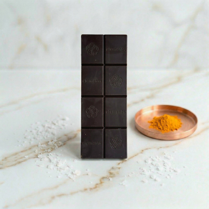 Dark chocolate bar pieces with sea salt crystals on marble, plus small dish of yellow spice.