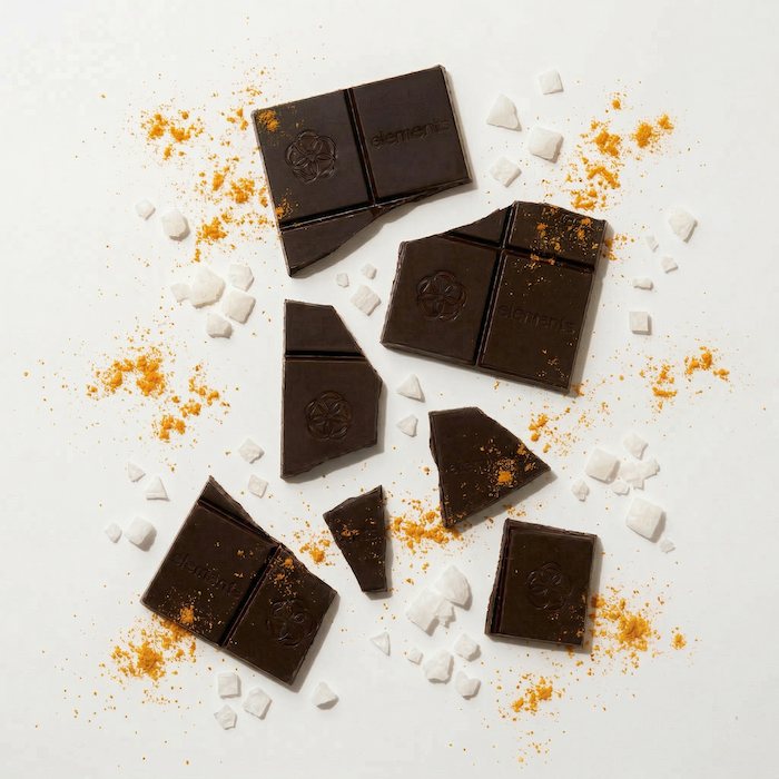 Broken dark chocolate squares with sea salt crystals and orange-yellow seasoning scattered.
