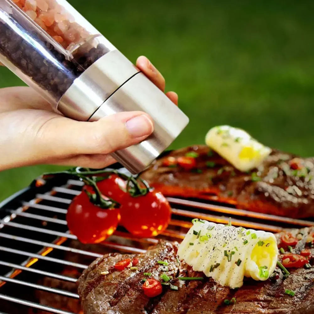 Manual stainless steel salt and pepper grinder held above grilled food