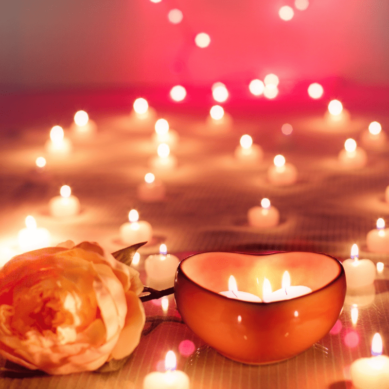 Heart-shaped scented candle in a dark glass holder with visible flame and rose