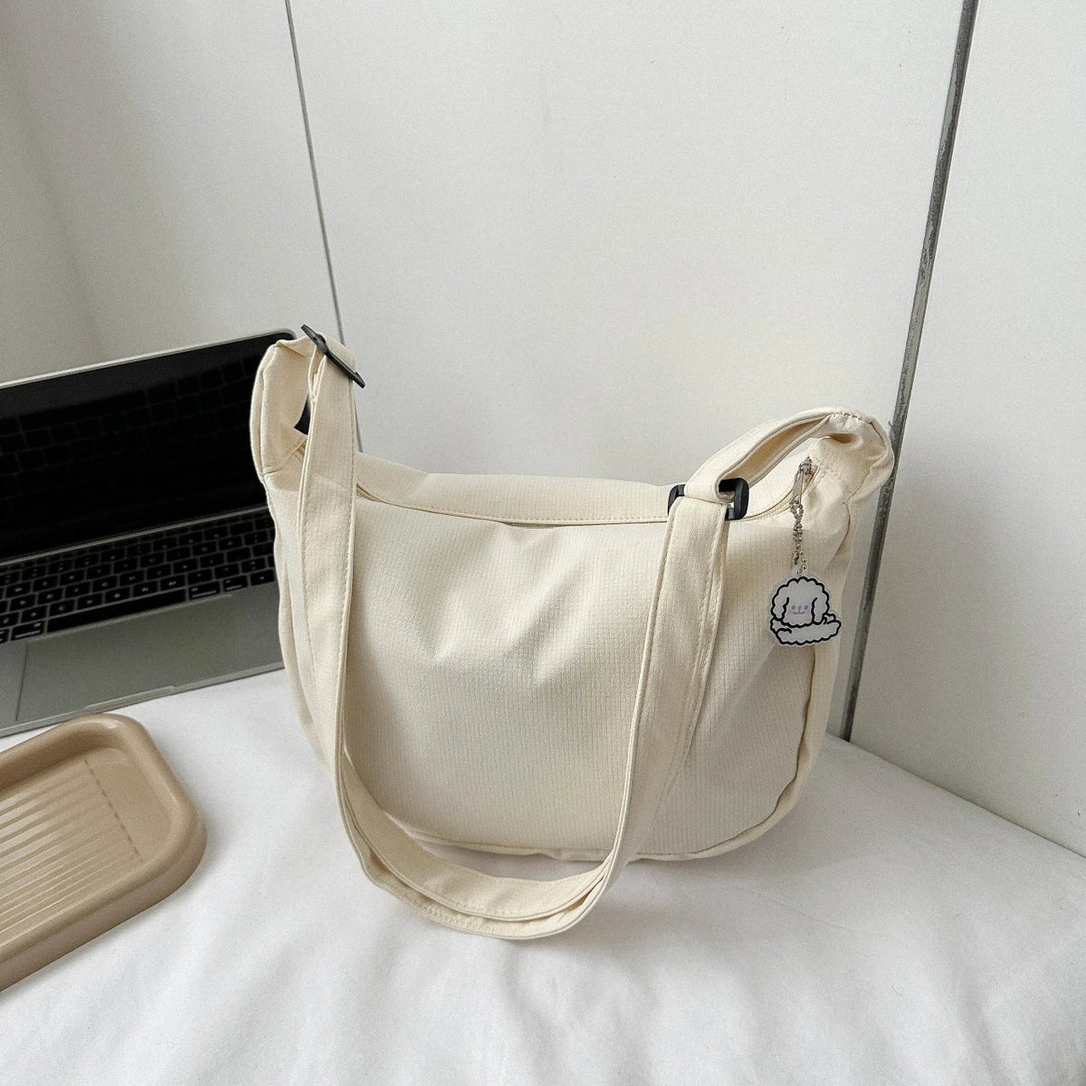 Cream crossbody bag with puppy pendant, zip-top, and adjustable shoulder strap