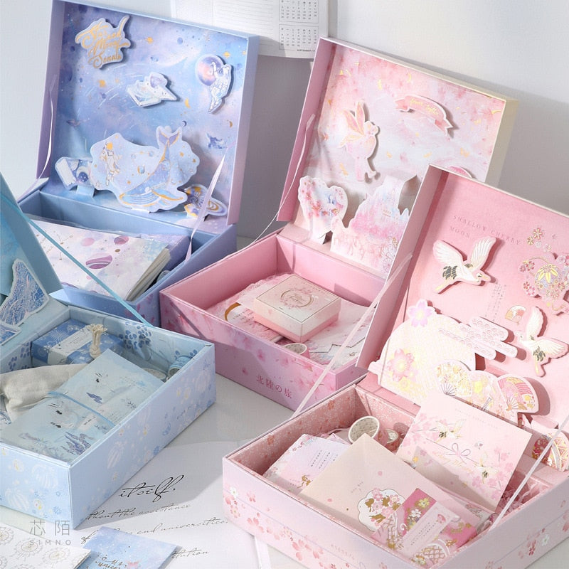 Assorted stationery gift sets in blue and pink boxes with cards, stickers, and tape