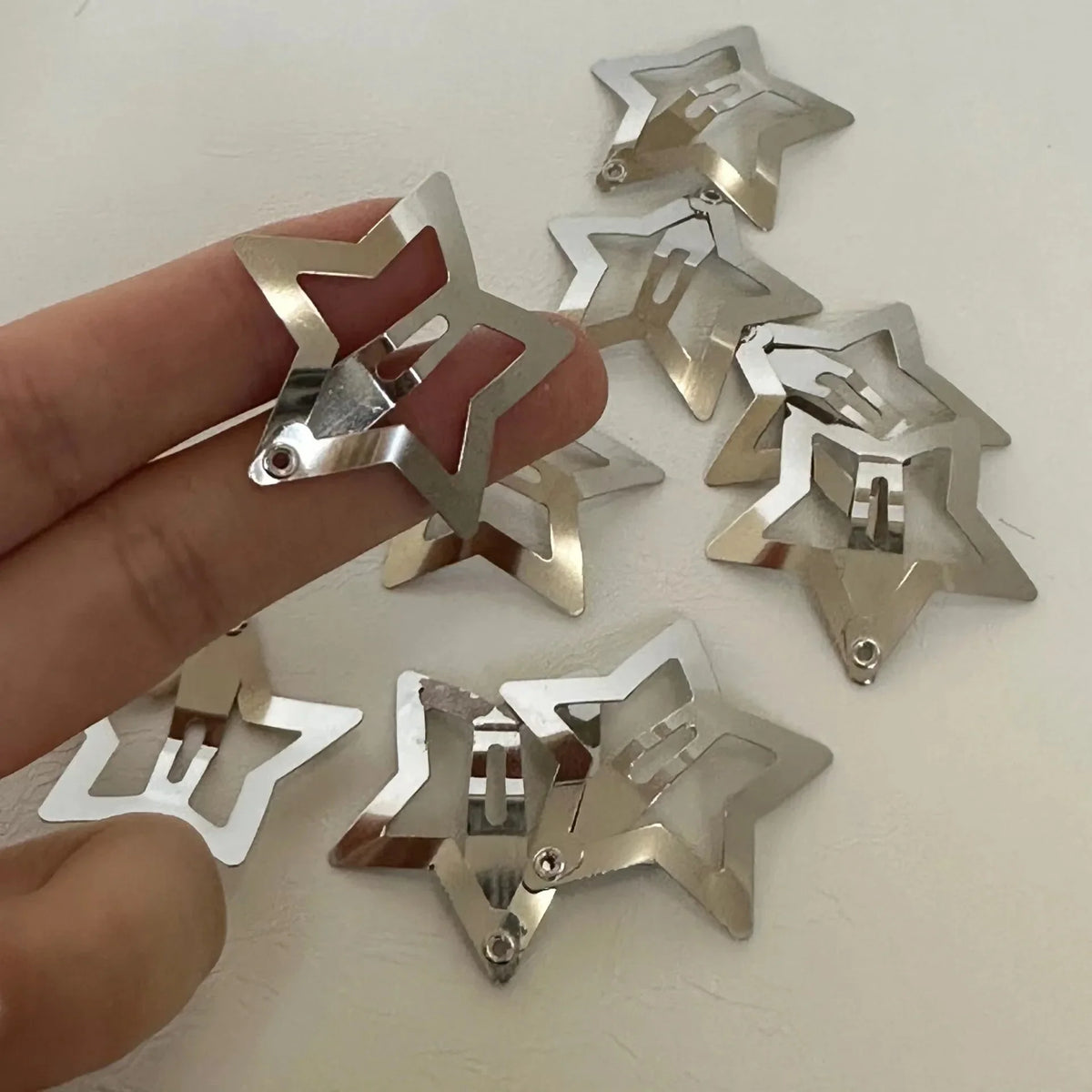 Silver star metal snap hair clips held in hand, multiple hinged star designs.
