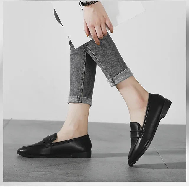 Black slip-on loafers with rounded toe, worn with cuffed gray jeans