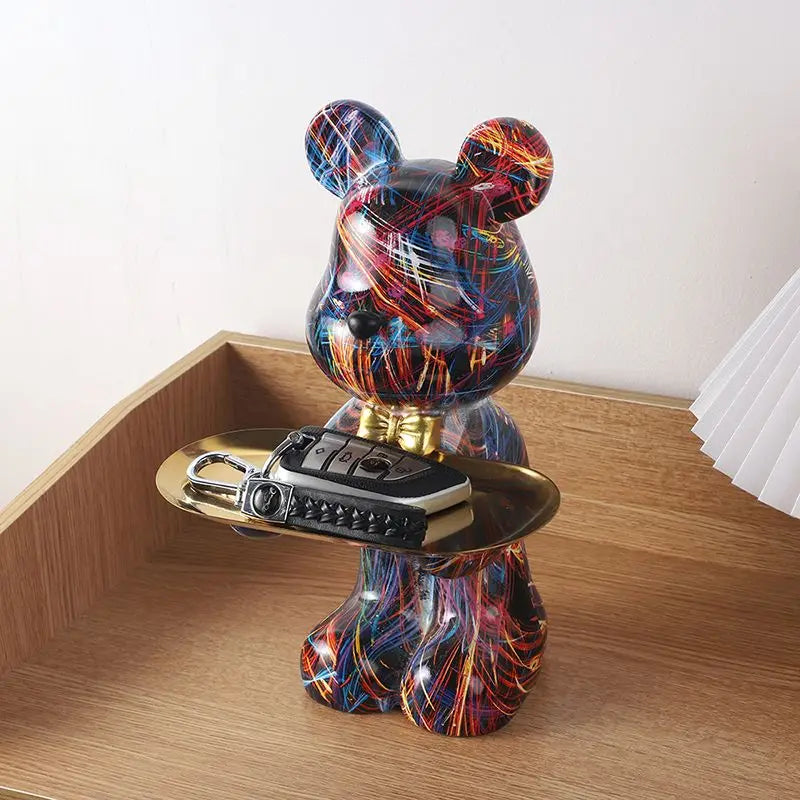 Colorful graffiti-style resin bear organizer with gold tray holding a black phone