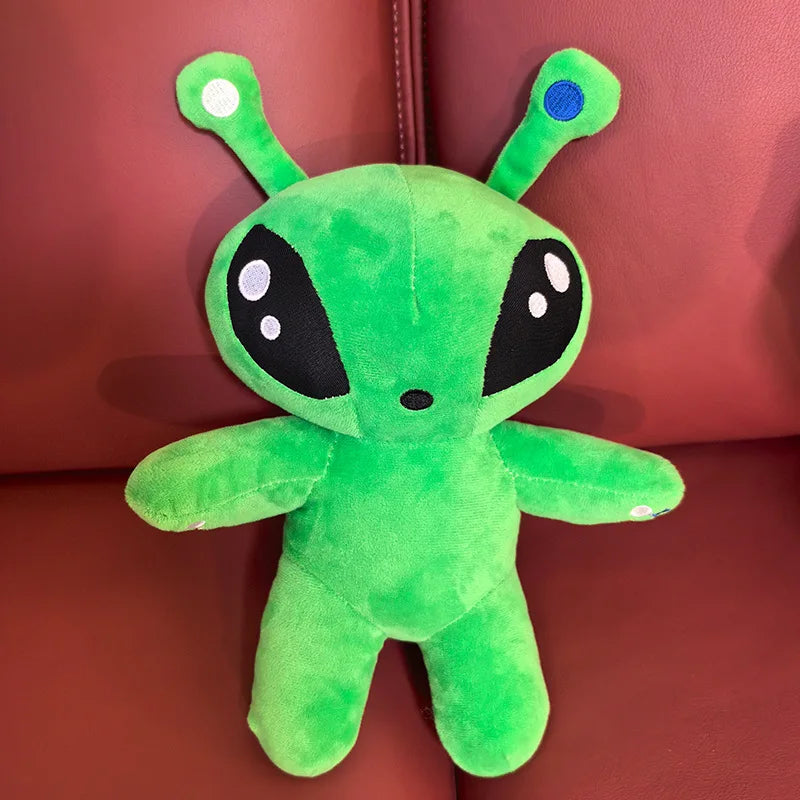 Green alien plush toy on red couch, round head with horn tentacles and black eyes