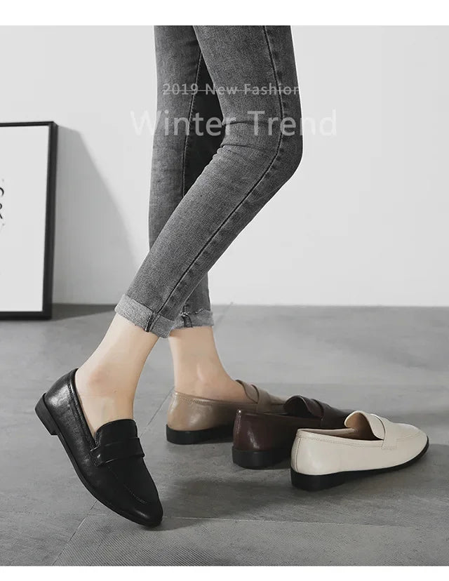 Women’s leather slip-on loafers in dark and off-white, round toe, low flat sole.
