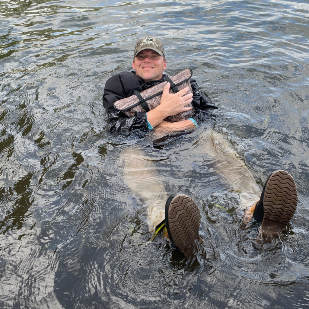 Waterproof floating cooler bag in camo floating on water with black shoulder strap