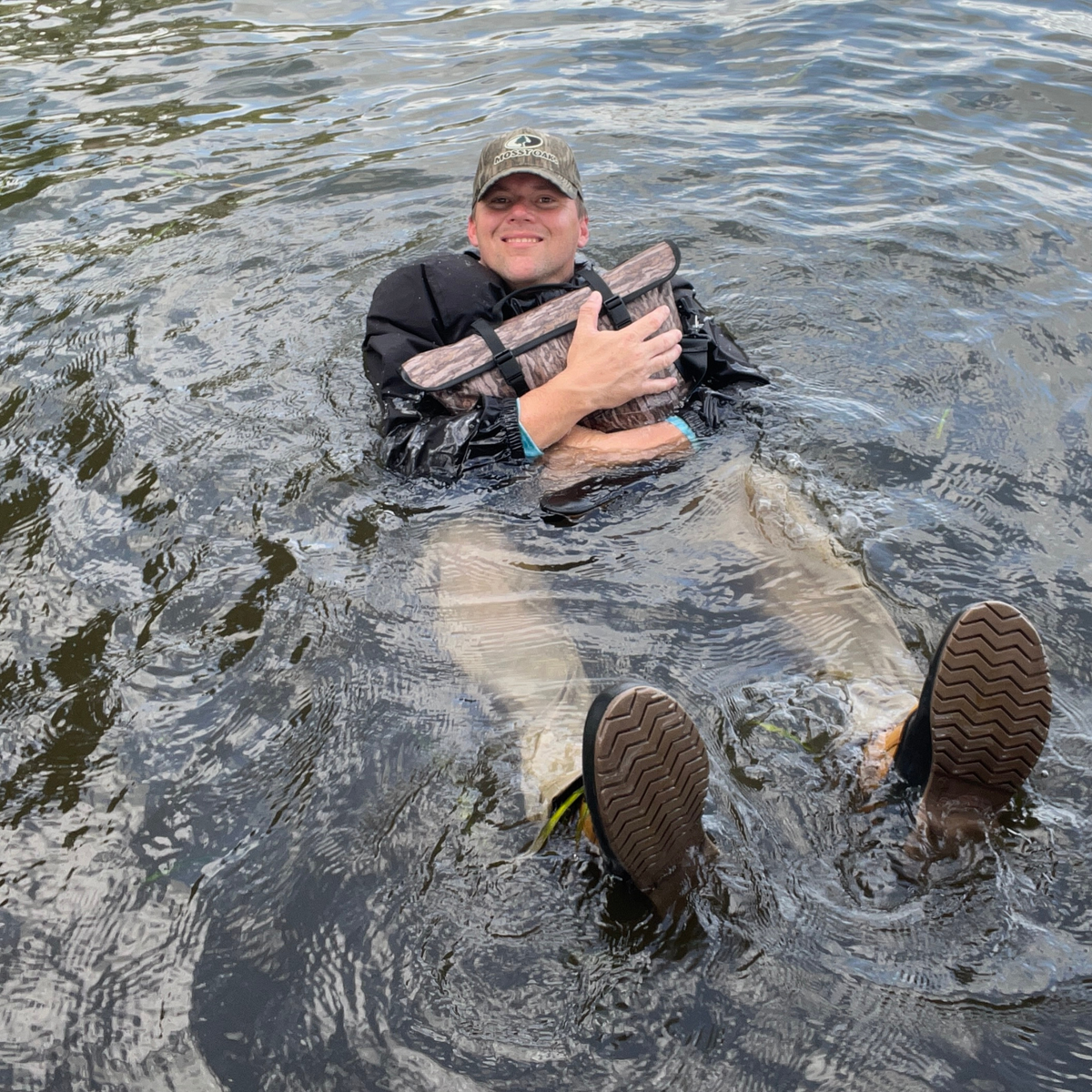 Waterproof floating cooler bag in camo floating on water with black shoulder strap